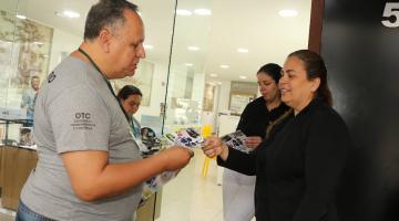 homem entrega folheto para mulher que está parada na porta de loja. #paratodosverem