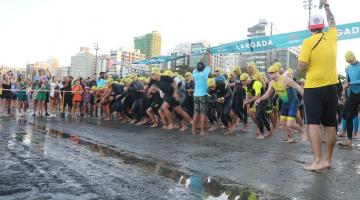 atletas dão largada na prova de natação. Eles estão na beira do mar e começam a correr em direção à água. #paratodosverem 