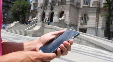 mão segura telefone celular diante da prefeitura. #paratodosverem