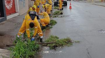 grupo de homens uniformizados está retirando mato junto à guia em rua. #paratodosverem 