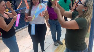 professores estão em pé em corredor lendo mensagens e fotos penduradas em fios. #paratodosverem 