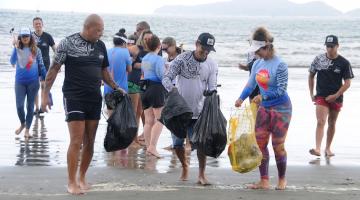 Praticantes estão na beira do mar com sacos onde estão depositados resíduos. 