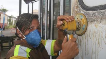 Mulher olha para a foto passando uma lixa elétrica sobre a área externa de um bonde. #paratodosverem