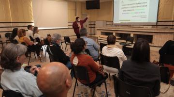 sala de reunião com um homem à frente de todos os que assistem. Ele aponta para um projetor na parede que tem informações sobre o programa Município Verde Azul. #paratodosverem 