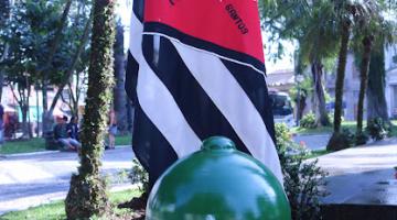 Modelo de capacete verde, dos antigos combatentes, sobre bandeira de São Paulo em mesa com toalha vermelha. #pratodosverem