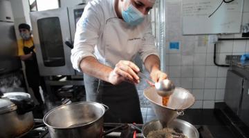 chefe de cozinha prepara prato e coloca o café líquido em risoto que está na panela. #paratodosverem