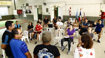 Professores sentados ouvindo quatro colegas na capacitação #pracegover 