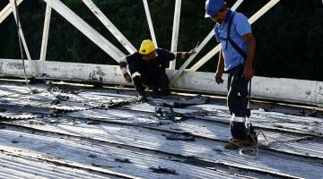 Homens trabalham em manutenção de telhado. #Pracegover