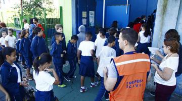 Crianças e pessoal de apoio da Defesa Civil nas dependências da escola. #Pracegover