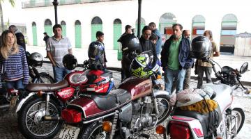 Motos raras em exposição na rua sob marquise. Público as observa