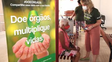 mulher conversa com idosa sentada, ao lado cartaz sobre doação de órgão. #paratodosverem