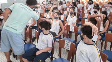 palestrante fala com criança em sala cheia de estudantes #paratodosverem