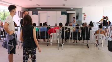 pessoas sentadas em frente a tenda aguardando atendimento cercadas pro gradis #paratodosverem