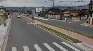 Trecho de avenida pavimentado, com faixa de pedestre e ciclovia no centro. #Pracegover