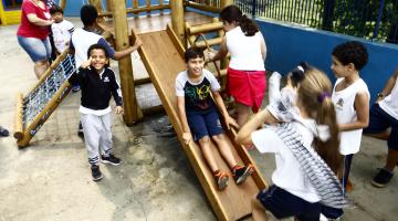 Crianças brincam no novo parque. Muitas delas estão em torno de um escorregador de madeira. #Pracegover