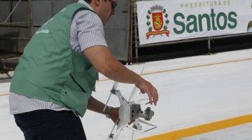 Homem vestindo colete de agente de combate à dengue  segura drone no meio do sambódromo.  #Pracegover