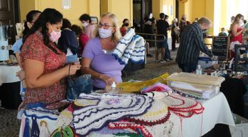 Mulheres olham artesanato em feira #paratodosverem
