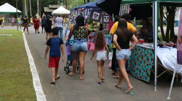 barracas de artesanato em meio a um jardim, com pessoas circulando. #paratodosverem 