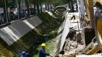 operários e máquina trabalham em borda de canal #pracegover 