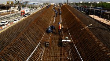 Estrutura de novo viaduto em construção. Armações em ferro estão aparentes. Homens trabalham na parte interna da estrutura