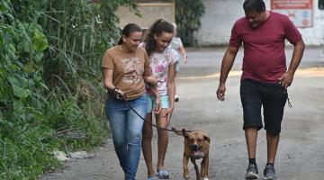 família de três pessoas caminha com cão. #paratodosverem