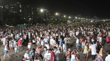 Praia lotada de pessoas à noite. #Pracegover