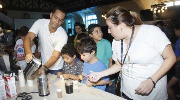 dois monitores ensinam preparação de café e crianças observam #paratodosverem