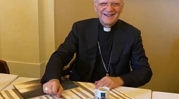 O arcebispo dom Angelo Vincenzo Zani está sentado a uma mesa. Há uma xícara de café na frente dele. #Pracegover