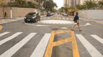 rotatória ao fundo, com carro passando, à esquerda, e mulher atravessando na faixa, à direita. #paratodosverem