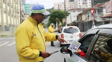 agente da cet uniformizado entrega folheto para pessoa dirigindo um taxo. Outro agente está à frente fazendo o mesmo. #paratodosverem