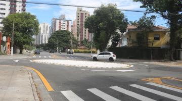 faixa de segurança em primeiro plano, calçada à esquerda e rotatória à frente com carro circulando. #paratodosverem