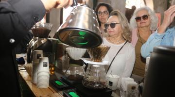 mão seguram bule e servem café para público. #paratodosverem