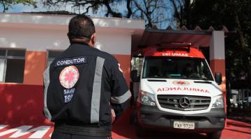 condutor uniformizado está de costas para a foto e de frente para a base do samu e para uma ambulância. #paratodosverem