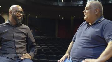 dois homens conversam lado a lado em palco. #paratodosverem