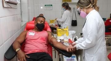 homem com braço esticado para doação de sangue ao lado de enfermeira #paratodosverem