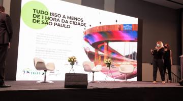 secretária fala no palco com viaduto de santos aparecendo no painel #paratodosverem