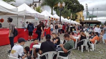 Barracas ao fundo e pessoas sentadas em mesa na rua #paratodosverem