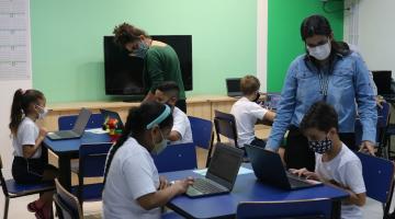 crianças mexem no computador e professoras orientam #paratodosverem