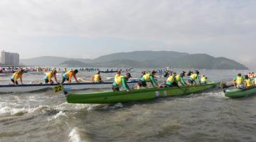 canoas estão entrando no mar com pessoas do lado de fora empurrando-as. São três canoas à vista. #paratodosverem