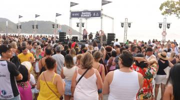 pessoas assistem show na ponta da praia com navio ao fundo. #paratodosverem