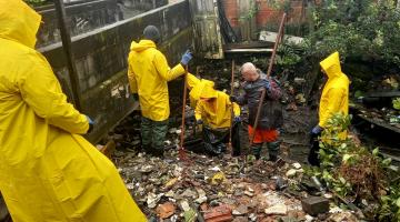 operários vestindo capas de chuva removem manualmente lixo de canal. #paratodosverem