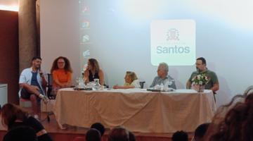 mesa de debates com seis pessoas sentadas e Wilma ao centro. #paratodosverem