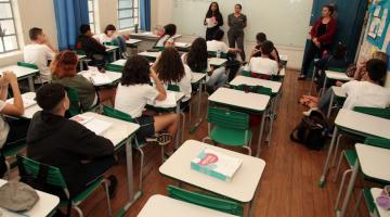 alunos estão tendo aula em sala. estão de costas para a foto. professores ao fundo em frente à lousa. #paratodosverem 