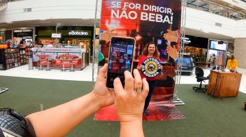 Mulher segura placa com a inscrição Motorista da Roda, embaixo de grande letreiro. #paratodosverem