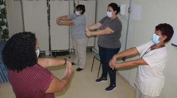 mulheres estão fazendo exercícios de alongamento com os braços em sala. #paratodosverem
