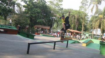 jovem faz manobra em uma espécie de corrimão próprio para skate. ele esta no ar, com os braços para cima. #paratodosverem