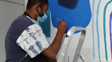 Homem faz pintura em parede da sala de ouvidoria na Subprefeitura dos Morros. #pracegover