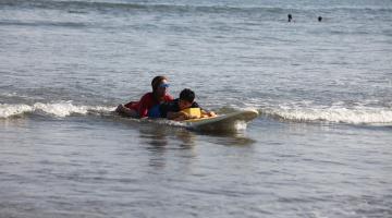 pessoa ajudando criança a surfar #paratodosverem