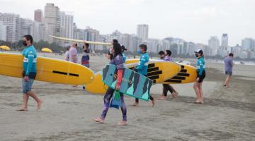 Surfistas seguram a prancha na areia da praia. #paratodosverem