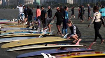 pranchas estão estendidas na areia. alunos se movimentam em torno. #paratodosverem